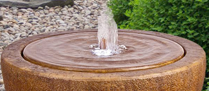 Outdoor garden fountain with water flowing into a circular basin surrounded by landscaping