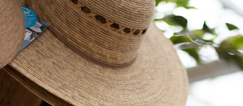 Straw gardening hat with woven detail hanging outdoors in a garden setting