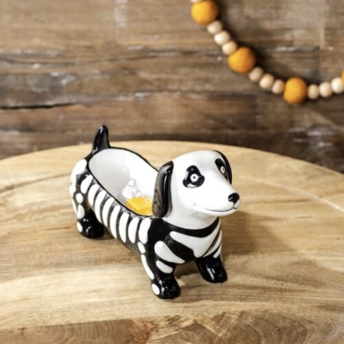 Black and white skeleton dog candy dish on a wooden tabletop with fall décor in the background.