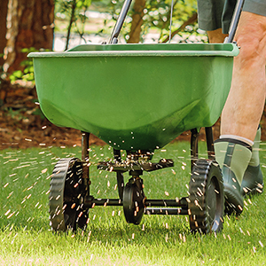 Lawn Spreader Applying Seed | Suburban Lawn & Garden Green lawn spreader applying grass seed or fertilizer across a healthy green lawn